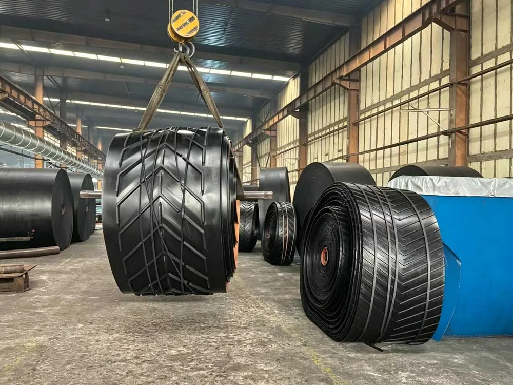 Large rolls of heavy-duty rubber conveyor belts stored in a manufacturing factory workshop